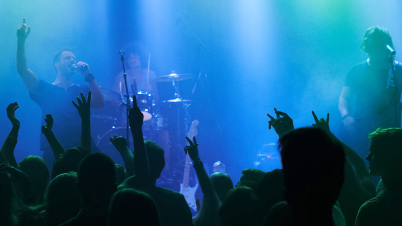 band on stage, crowd with hands up and blue lights